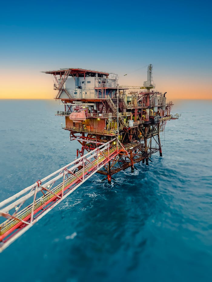 about-img Aerial view of an offshore oil rig surrounded by the ocean at sunset, under a clear sky.