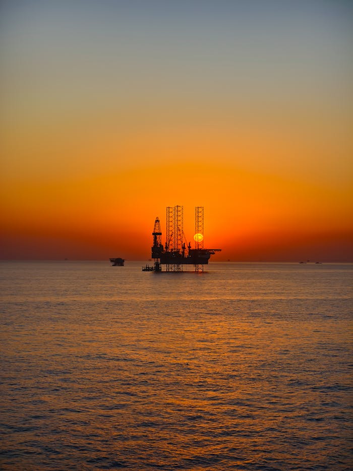 services-02 Silhouette of an oil rig against a vibrant sunset over the ocean, capturing the essence of industrial beauty.