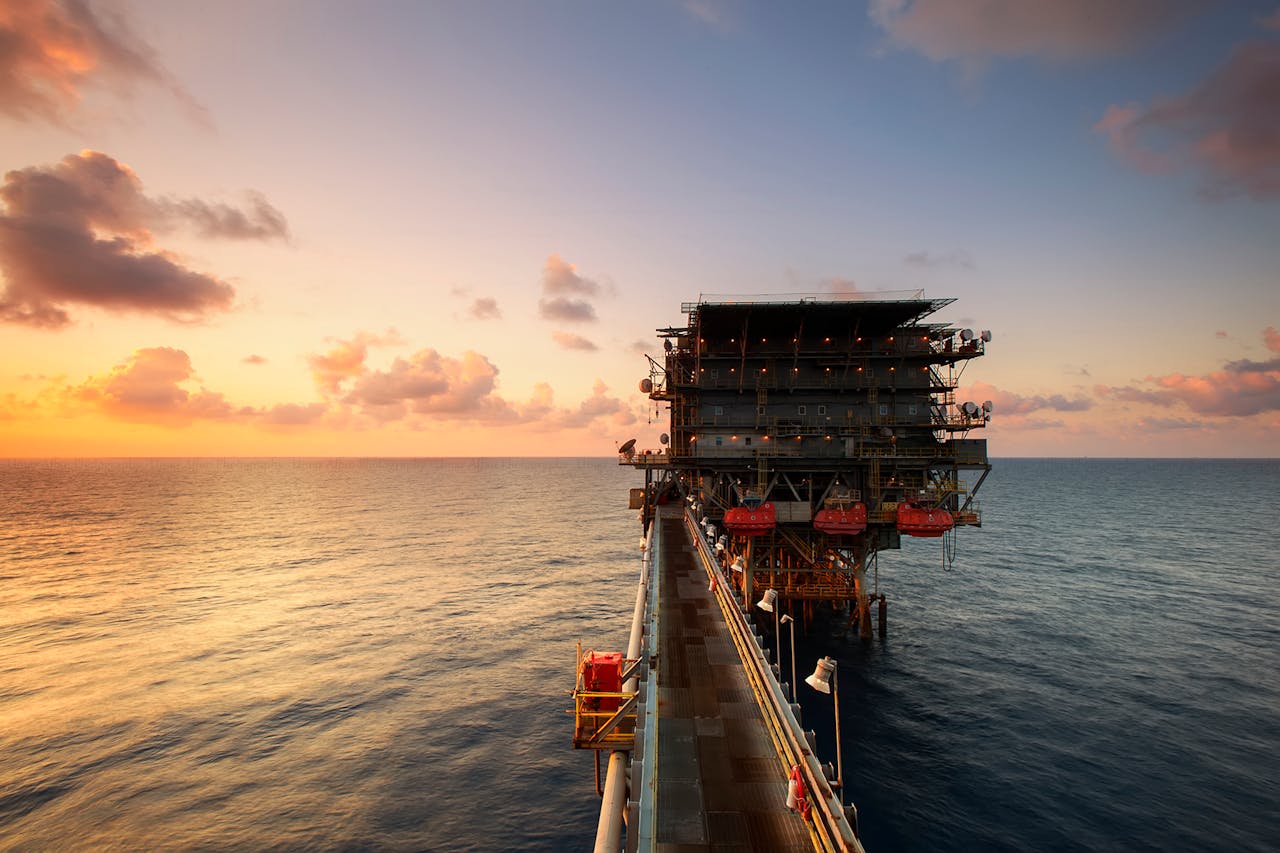 services-01 A breathtaking view of an oil platform on the ocean at sunset, showcasing industrial beauty.