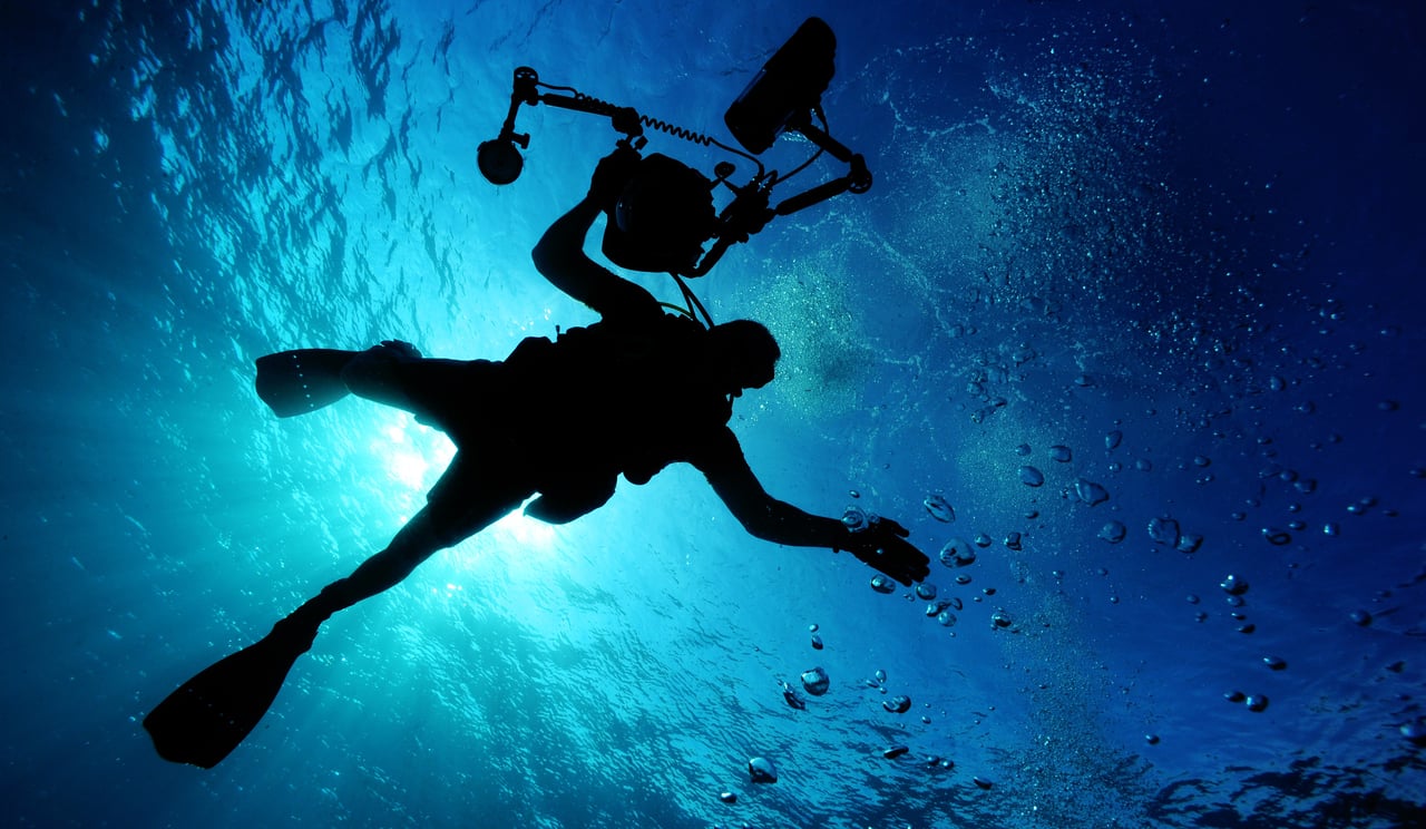 about-02 Silhouette of a diver filming underwater, capturing the serene oceanic environment.